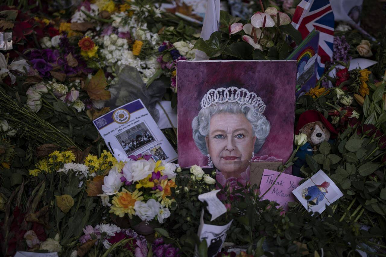 A painting of the Queen Elizabeth II is seen next to flowers at Green Park, near Buckingham Palace, in London, Sunday, Sept. 18, 2022. The Queen will lie in state in Westminster Hall for four full days before her funeral on Monday Sept. 19. (AP Photo/Felipe Dana)