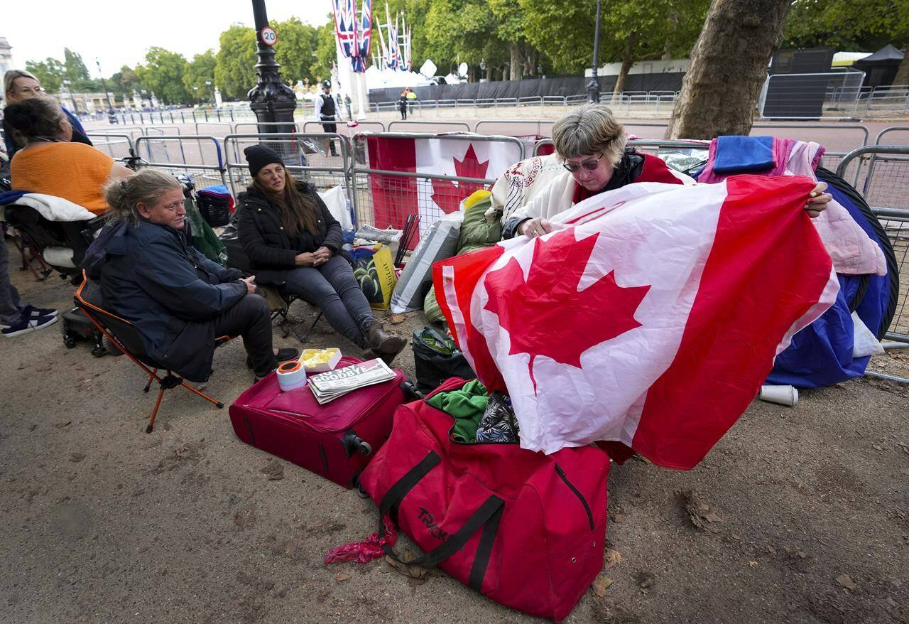 Bernadette Christie, of Grand Prairie, Alta., looks for a Canadian pin on a flag at the gates of Buckingham Palace in London, Friday, Sept. 16, 2022. For some Canadians, Queen Elizabeth’s funeral today will evoke a range of emotions while for others it is a distant event that they are likely to miss. THE CANADIAN PRESS/Nathan Denette