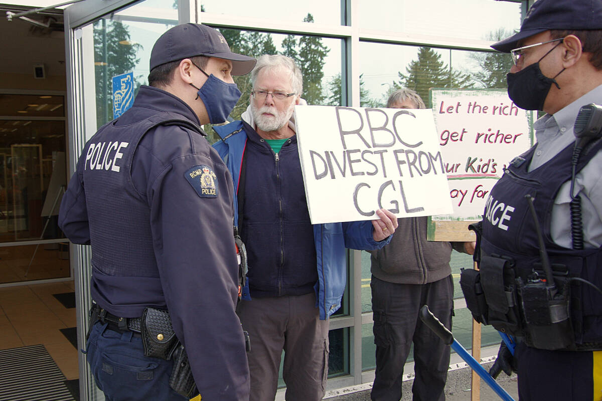 Nanaimo RCMP officers speak with Vic Brice during a protest at RBC on April 7, when he glued his hand to the handle of the bank branch’s entrance. (News Bulletin file photo)