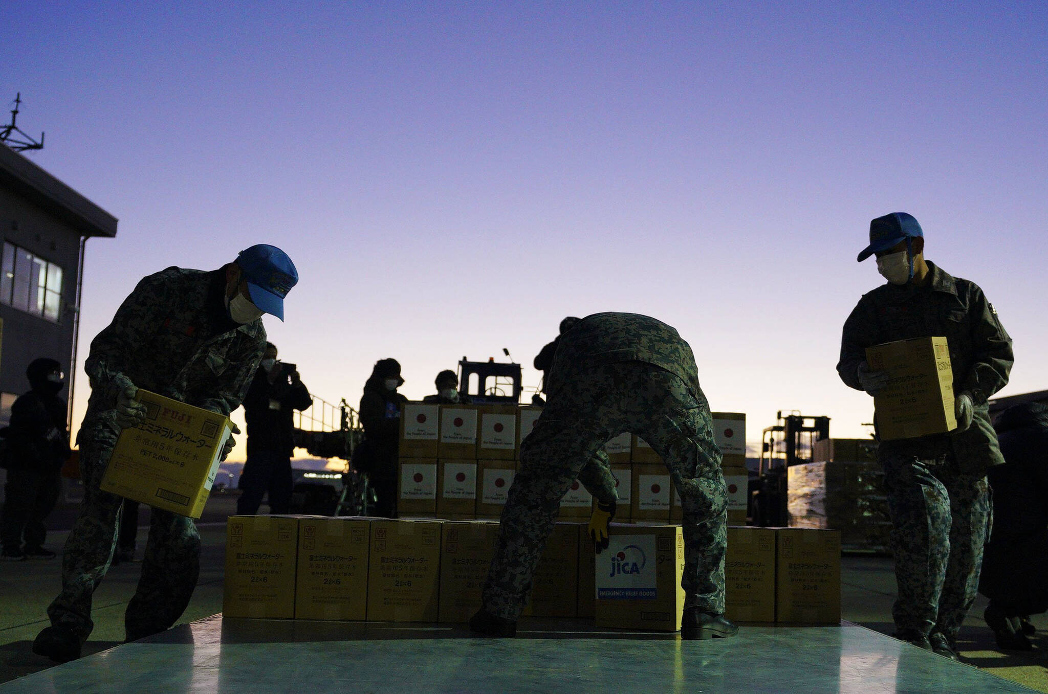 Members of Japan’s Air Self-Defense Force help load boxes of water into an airplane at an airbase in Komaki, central Japan, Thursday, Jan. 20, 2022, as they were preparing to take off for Australia on their way to Tonga to transport the emergency relief goods, following Saturday’s volcanic eruption near the Pacific nation. Japan’s Defense Ministry said it would send emergency relief, including drinking water and equipment for cleaning away volcanic ash. (Kyodo News via AP)