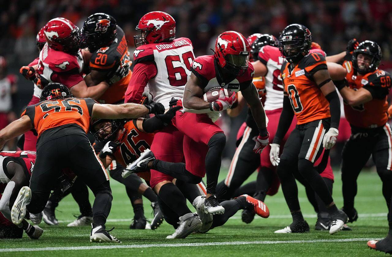 Calgary Stampeders’ Ka’Deem Carey, centre, runs past B.C. Lions’ David Menard (56) and Ben Hladik (46) to score a touchdown during the first half of CFL football game in Vancouver, on Saturday, Sept. 24, 2022. THE CANADIAN PRESS/Darryl Dyck