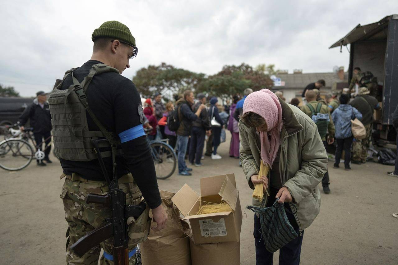 A Ukrainian serviceman of Sophia battalion distributes humanitarian aid to a local woman in the recently liberated town of Izium, Ukraine, Sunday, Oct. 2, 2022. (AP Photo/Evgeniy Maloletka)