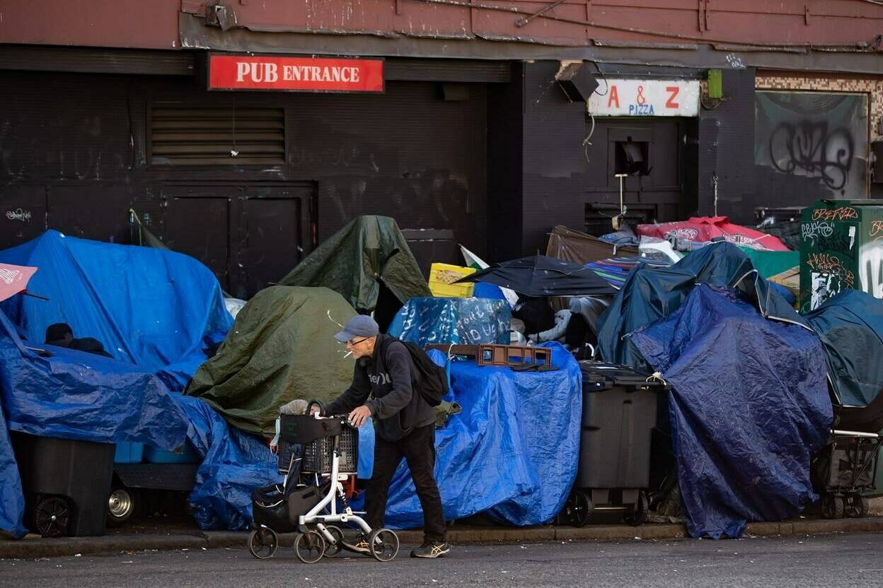 A man using a rolling walker walks on the street past tents setup on the sidewalk at a sprawling homeless encampment on East Hastings Street in the Downtown Eastside of Vancouver, on August 16, 2022. The city has been clearing the street in accordance with a safety order by the city’s fire chief. THE CANADIAN PRESS/Darryl Dyck