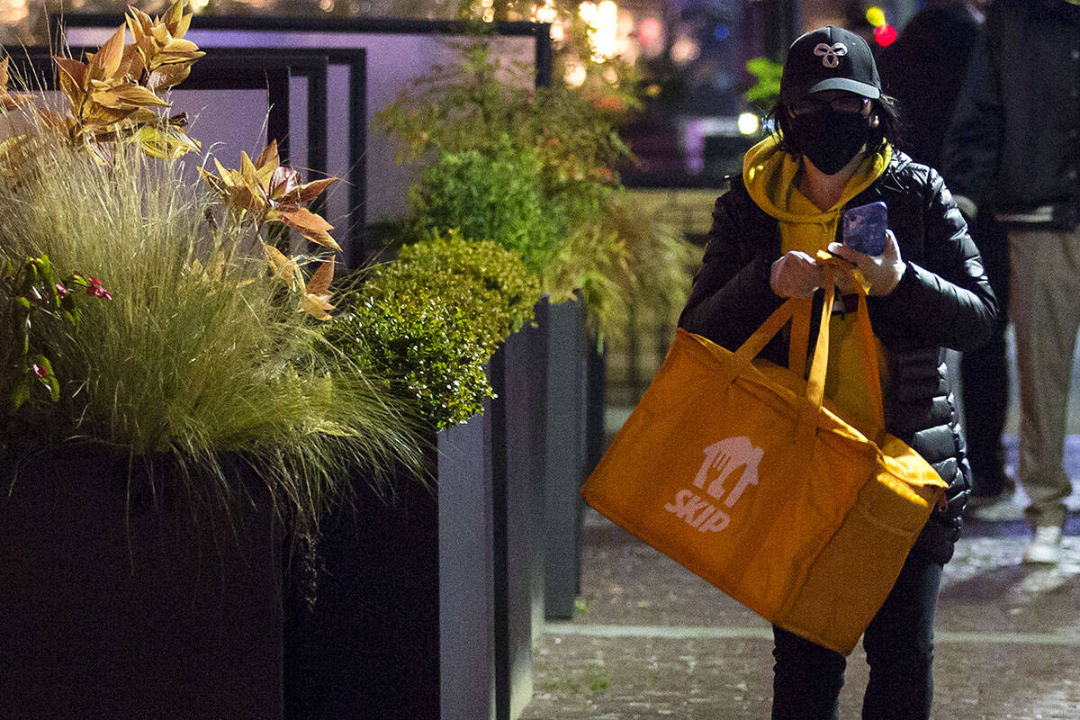 A food delivery person wears a face mask as they walk away from a downtown Vancouver restaurant with a pick-up on Dec. 3, 2020. The B.C. government is aiming to cap food delivery fees in the province permanently. THE CANADIAN PRESS/Marissa Tiel