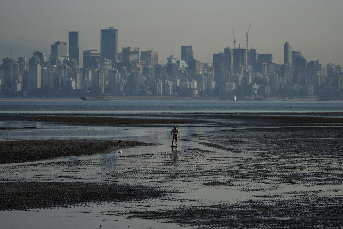 A man jumps on a skimboard while riding on tidal pools at Spanish Banks as smoke from wildfires burning in B.C. and in the U.S. hangs over the downtown core, in Vancouver, B.C., Thursday, Oct. 6, 2022. THE CANADIAN PRESS/Darryl Dyck