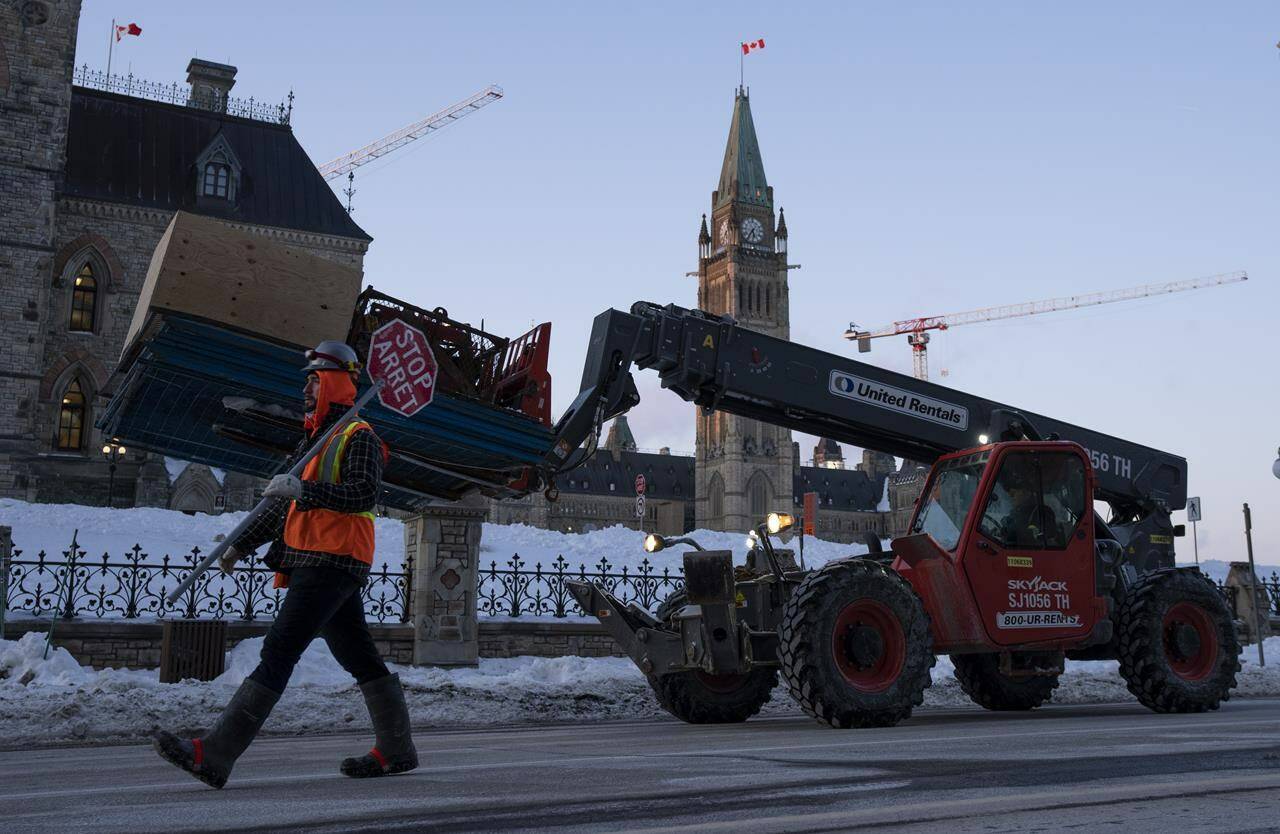 Workers use heavy equipment to remove temporary fencing and supplies from the parliamentary precinct, Wednesday, Feb. 23, 2022 in Ottawa. THE CANADIAN PRESS/Adrian Wyld