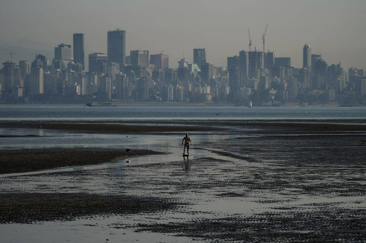 A man jumps on a skimboard while riding on tidal pools at Spanish Banks as smoke from wildfires burning in B.C. and in the U.S. hangs over the downtown core, in Vancouver, B.C., Thursday, Oct. 6, 2022. Firefighters in West Vancouver are responding to a what they describe as a wildfire at the top of the Caulfeild neighbourhood on the lower slopes of Cypress Falls Park. THE CANADIAN PRESS/Darryl Dyck