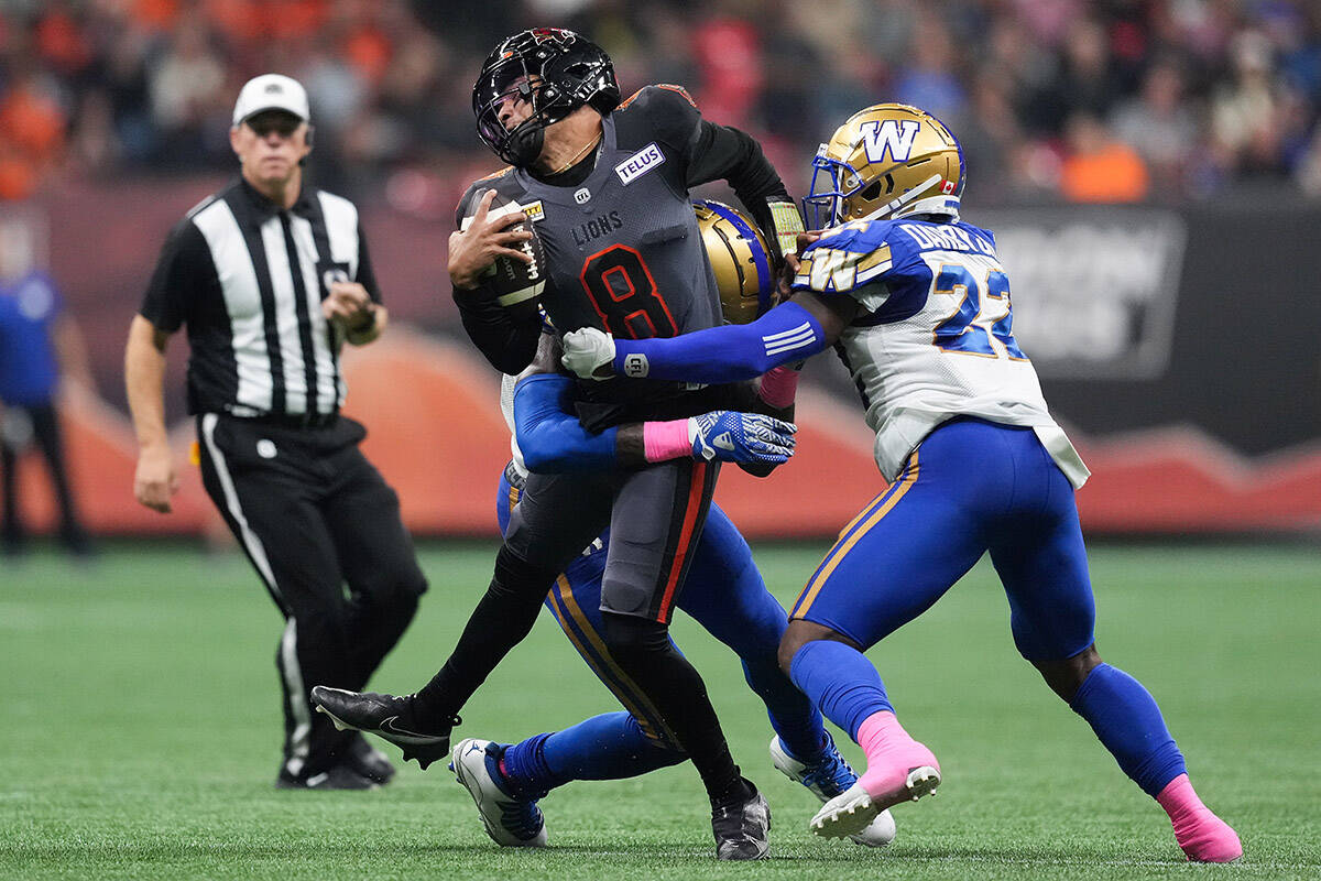 B.C. Lions quarterback Vernon Adams Jr. (8) is hit by Winnipeg Blue Bombers’ Willie Jefferson, back left, as he’s tackled by him and Alden Darby Jr. (22) during the first half of a CFL football game in Vancouver, on Saturday, October 15, 2022. THE CANADIAN PRESS/Darryl Dyck