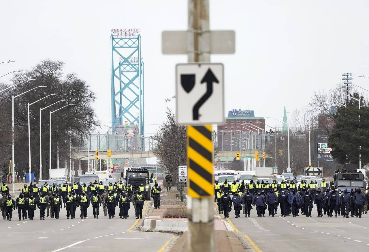 Police walk the line to remove all truckers and supporters after a court injunction gave police the power to enforce the law after protesters blocked the access leading from the Ambassador Bridge, linking Detroit and Windsor, as truckers and their supporters continue to protest against COVID-19 vaccine mandates and restrictions, in Windsor, Ont., Sunday, Feb. 13, 2022. THE CANADIAN PRESS/Nathan Denette