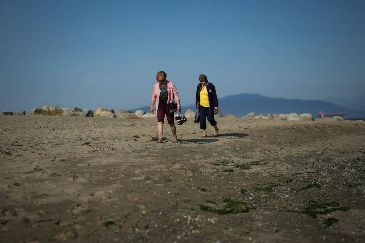 Two women carry their shoes as they walk together at Spanish Banks Beach during a stretch of unseasonably warm weather in Vancouver, B.C., Thursday, Oct. 6, 2022. THE CANADIAN PRESS/Darryl Dyck