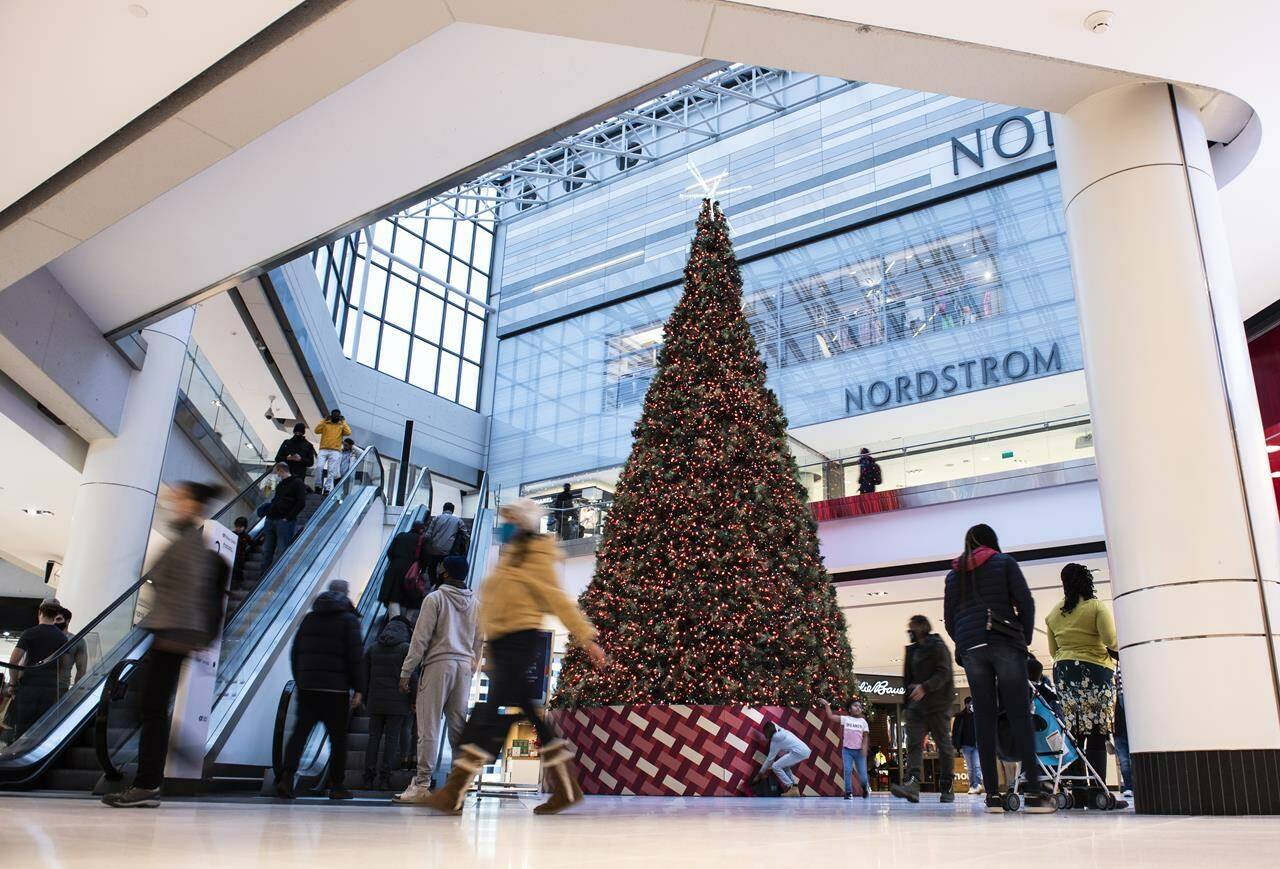 People pass a large Christmas tree as they go shopping on Christmas Eve at a mall in Ottawa on Dec. 24, 2020. A new report from Deloitte Canada says holiday spending in Canada is expected to drop this year as inflation shrinks consumer buying power and economic uncertainty looms over household finances. THE CANADIAN PRESS/Justin Tang