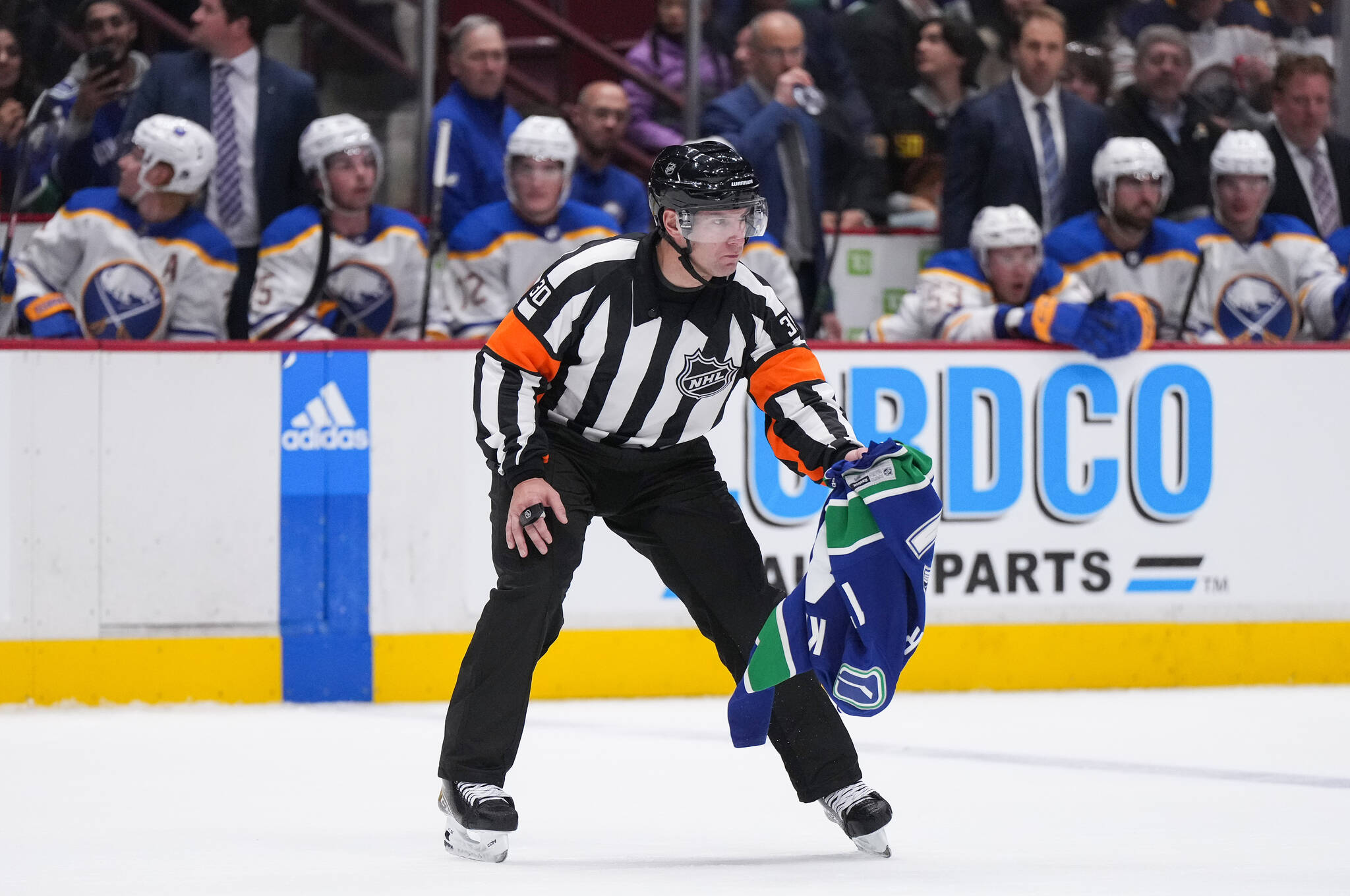 Referee Kendrick Nicholson picks up a Vancouver Canucks jersey that was thrown onto the ice by a fan as the team plays the Buffalo Sabres during the third period of an NHL hockey game in Vancouver, on Saturday, October 22, 2022. THE CANADIAN PRESS/Darryl Dyck