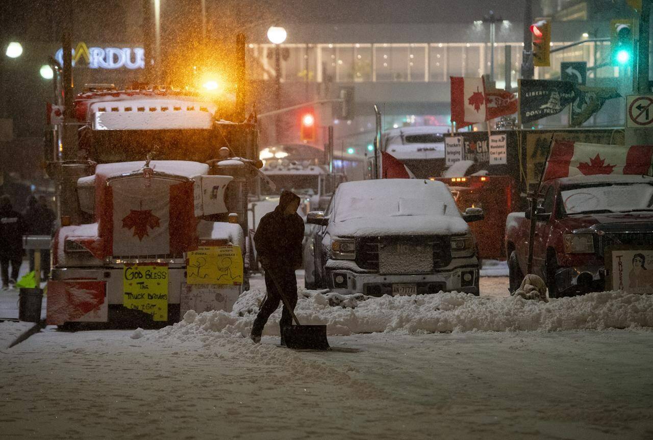 A protester shovels snow in front of parked semi-trailer and pickup trucks on Rideau Street, on the 21st day of a protest against COVID-19 measures that has grown into a broader anti-government protest, in Ottawa, on Thursday, Feb. 17, 2022. The commission investigating the government’s use of the federal Emergencies Act last winter will hear this week from the protesters who organized the occupation of downtown Ottawa. THE CANADIAN PRESS/Justin Tang