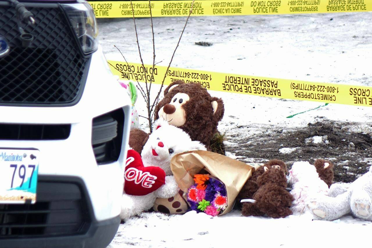 Flowers and stuffed animals are placed on the side of the road as police and fire investigators look over the scene of Wednesday evening’s house fire that left four children dead in Thompson, Man., Thursday, Oct. 27, 2022. THE CANADIAN PRESS/Ian Graham