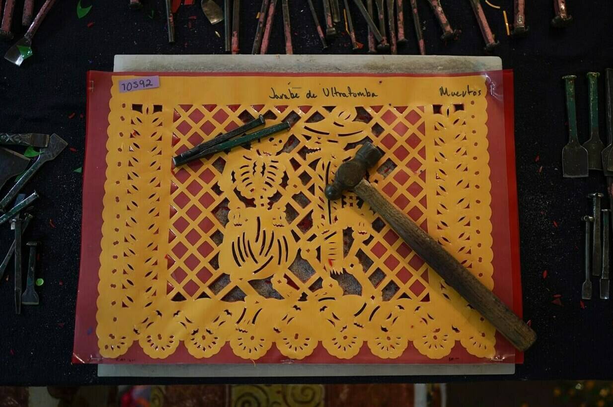 Tools used for “papel picado”, the traditional manufacture of tissue paper cut-out decorations, long used in altars for the Day of the Dead, lay on top of a stencil in a workshop in Xochimilco, a borough of Mexico City, Thursday, Oct. 27, 2022. Begun in the 1800s, experts say using tissue paper is probably a continuation of a far older pre-Hispanic tradition of painting ceremonial figures on paper made of fig-bark sheets. Mexican artisans adopted imported tissue paper because it was cheap and thin enough so that, with sharp tools, extreme care and a lot of skill, dozens of sheets can be cut at the same time. (AP Photo/Eduardo Verdugo)