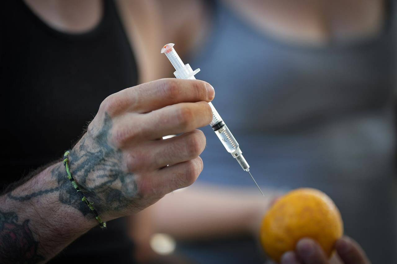 A person holds a syringe and an orange while learning how to administer Naloxone to an overdose victim, during an International Overdose Awareness Day gathering in Surrey, B.C., on Wednesday, Aug. 31, 2022. THE CANADIAN PRESS/Darryl Dyck