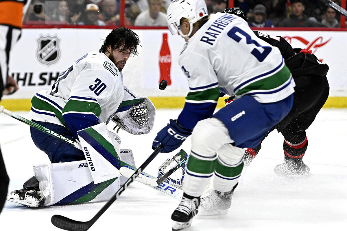 Vancouver Canucks goaltender Spencer Martin (30) watches the puck after losing his helmet as defenceman Jack Rathbone (3) defends against Ottawa Senators left wing Brady Tkachuk (7), behind, during second period NHL hockey action in Ottawa, on Tuesday, Nov. 8, 2022. THE CANADIAN PRESS/Justin Tang