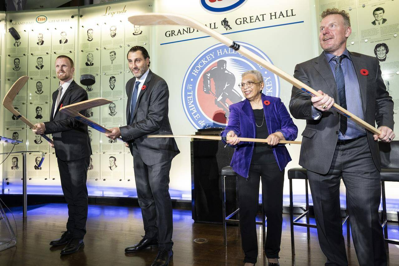 Daniel Sedin, left to right, Roberto Luongo, Herb Carnegie’s daughter Bernice Carnegie, and Daniel Alfredsson pose with sticks during a ceremony at the Hockey Hall of Fame in Toronto, Friday, Nov. 11, 2022. THE CANADIAN PRESS/Chris Young