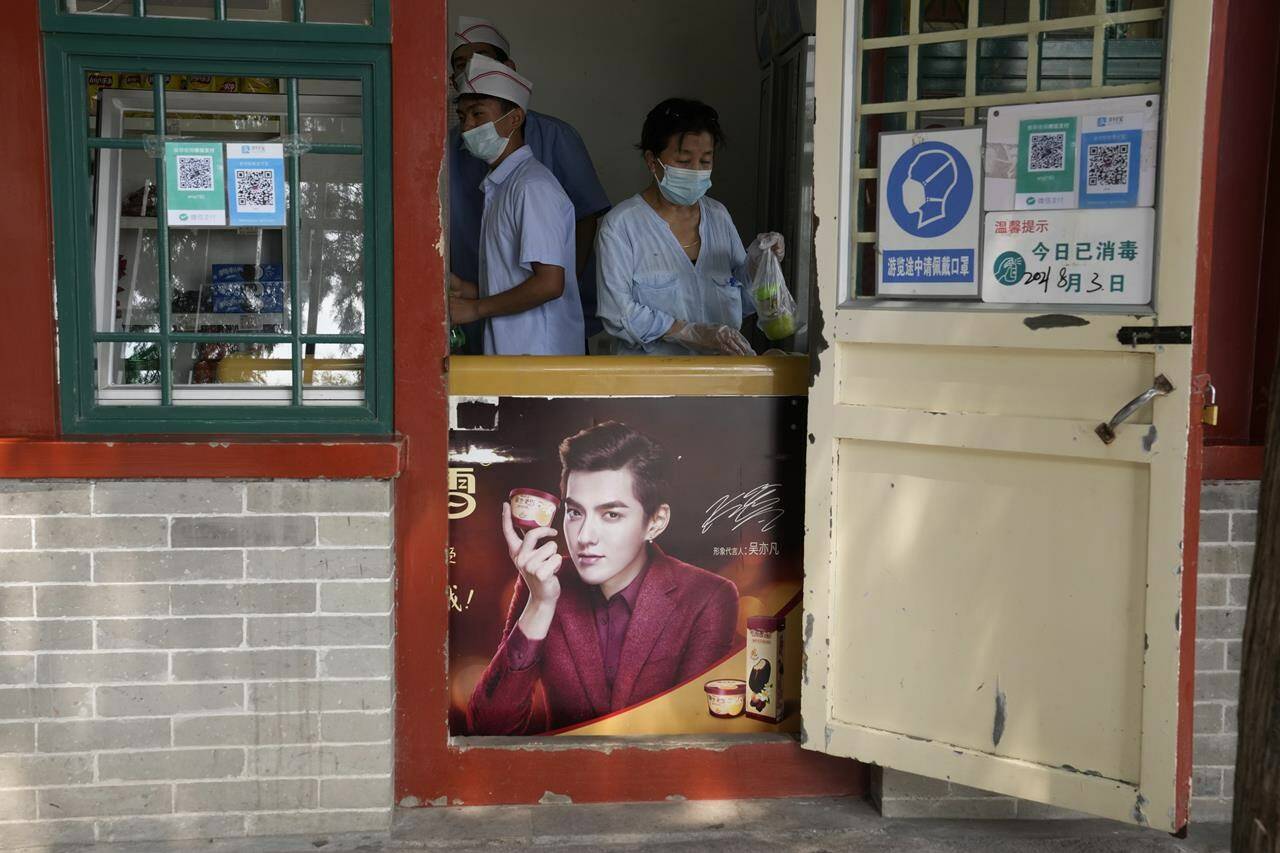 FILE - Food vendors work behind an ice cream fridge with an advertisement featuring Chinese-Canadian pop star Kris Wu in Beijing on Aug. 3, 2021. A Beijing court on Friday, Nov. 25, 2022 sentenced Chinese-Canadian pop star Kris Wu to 13 years in prison on charges including rape. (AP Photo/Ng Han Guan, File)