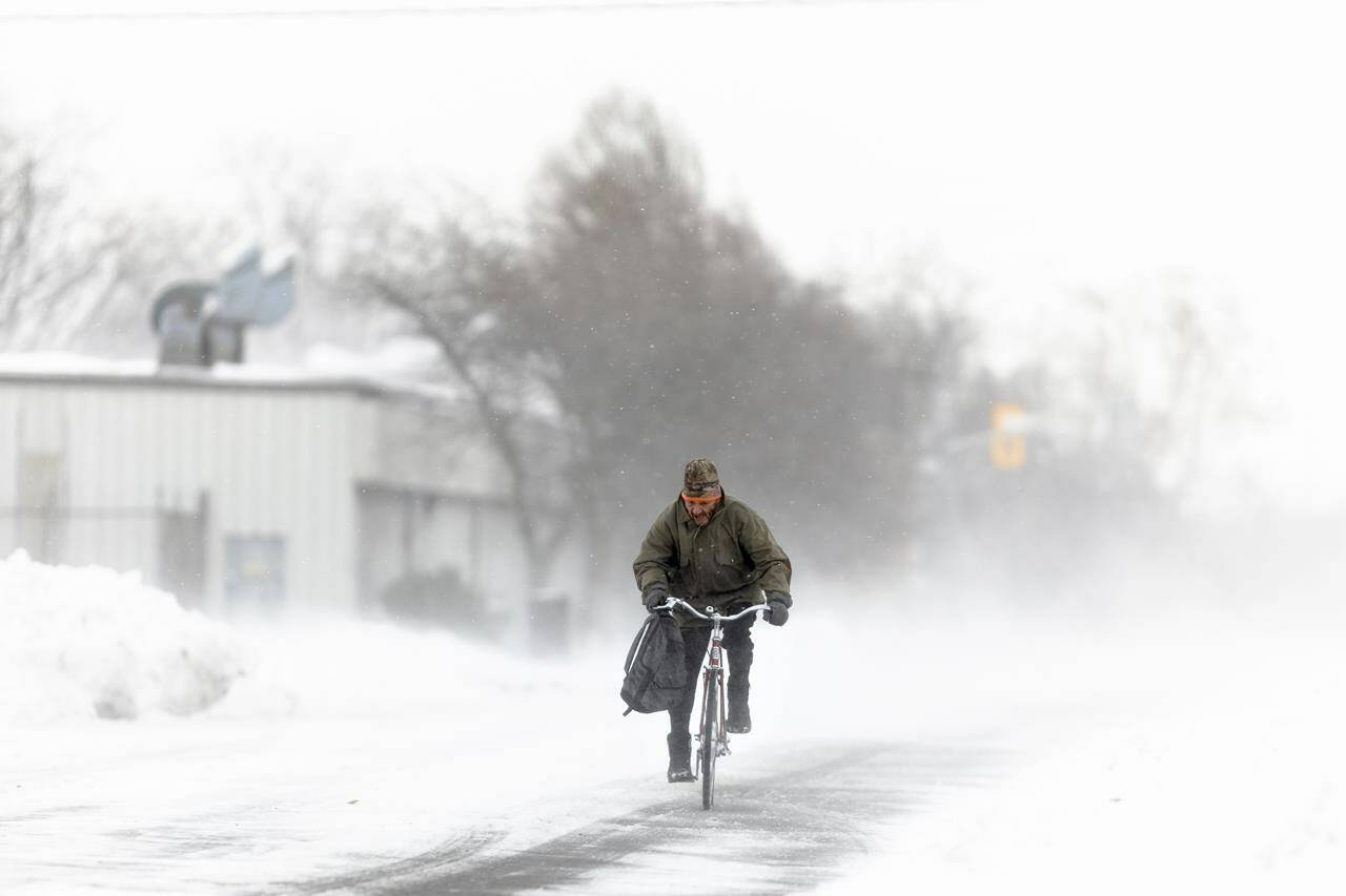 A man rides his bike down the street in Fort Erie, Ont., during an early winter storm that delivered high winds and large amounts of snow across southern Ontario and western New York, Saturday, Nov. 19, 2022. Canadians enjoying a brief relief from the onset of winter-like conditions may want to enjoy the temperatures while they can because The Weather Network is forecasting a colder than normal start to winter across most of the country. THE CANADIAN PRESS/Nick Iwanyshyn