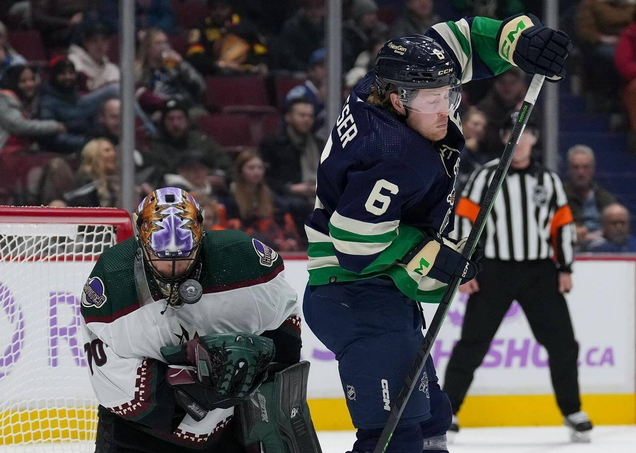 Arizona Coyotes goalie Karel Vejmelka, left, of the Czech Republic, is struck in the mask by the puck as Vancouver Canucks’ Brock Boeser stands in front of him during the first period of an NHL hockey game in Vancouver, on Saturday, December 3, 2022. THE CANADIAN PRESS/Darryl Dyck