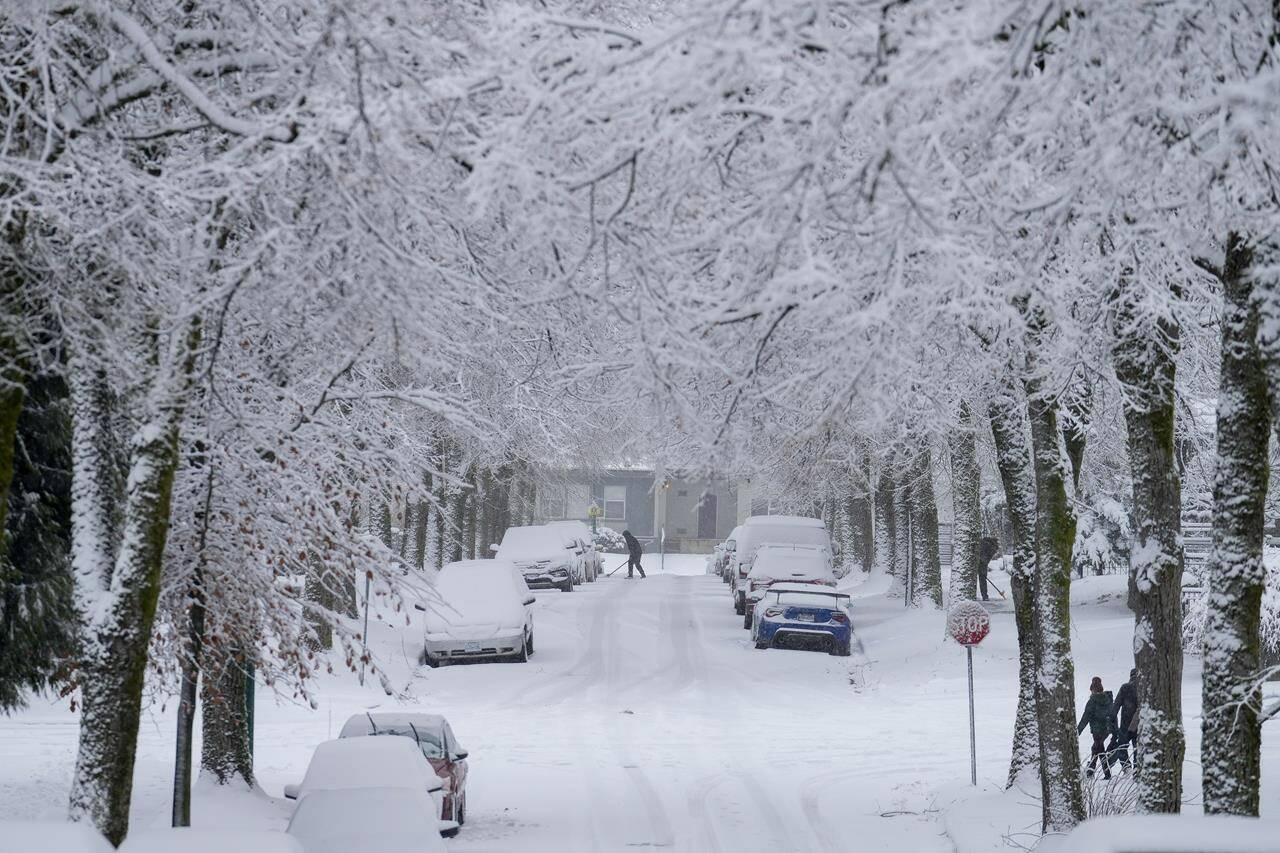 A person uses a shovel to clear snow from around a parked vehicle as snow falls in Vancouver, on Sunday, December 18, 2022. Weather alerts blanket most of British Columbia, Yukon and a large portion of Alberta as a bitterly cold system sweeps across those regions and another round of snow threatens southern B.C. THE CANADIAN PRESS/Darryl Dyck