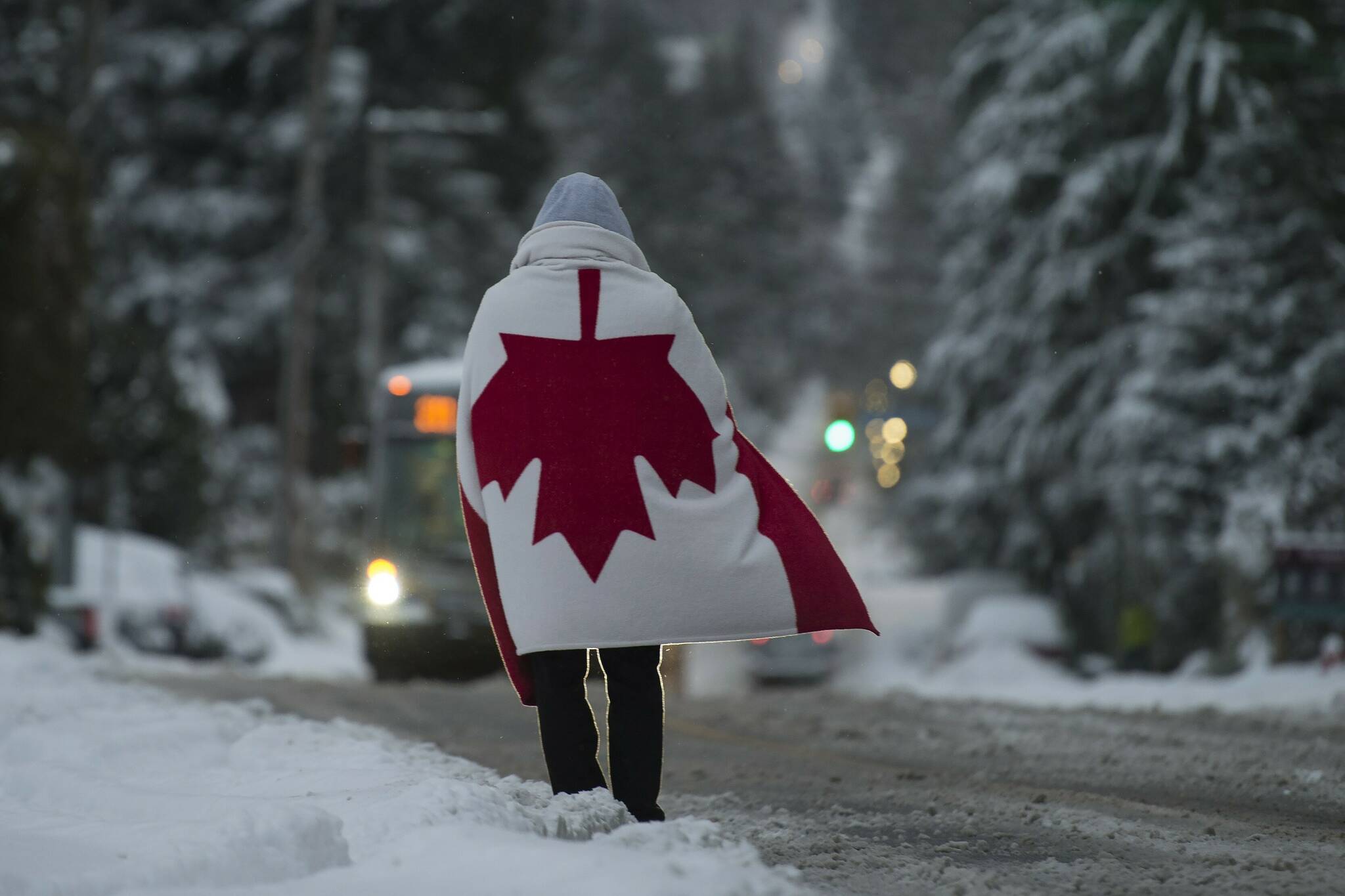 A man wearing a Canadian flag stands in the middle of a snow-covered road while he waits for the bus in North Vancouver, B.C., Wednesday, January 15, 2020. Vancouver and the lower mainland have been hit with cold temperatures and snow. THE CANADIAN PRESS/Jonathan Hayward