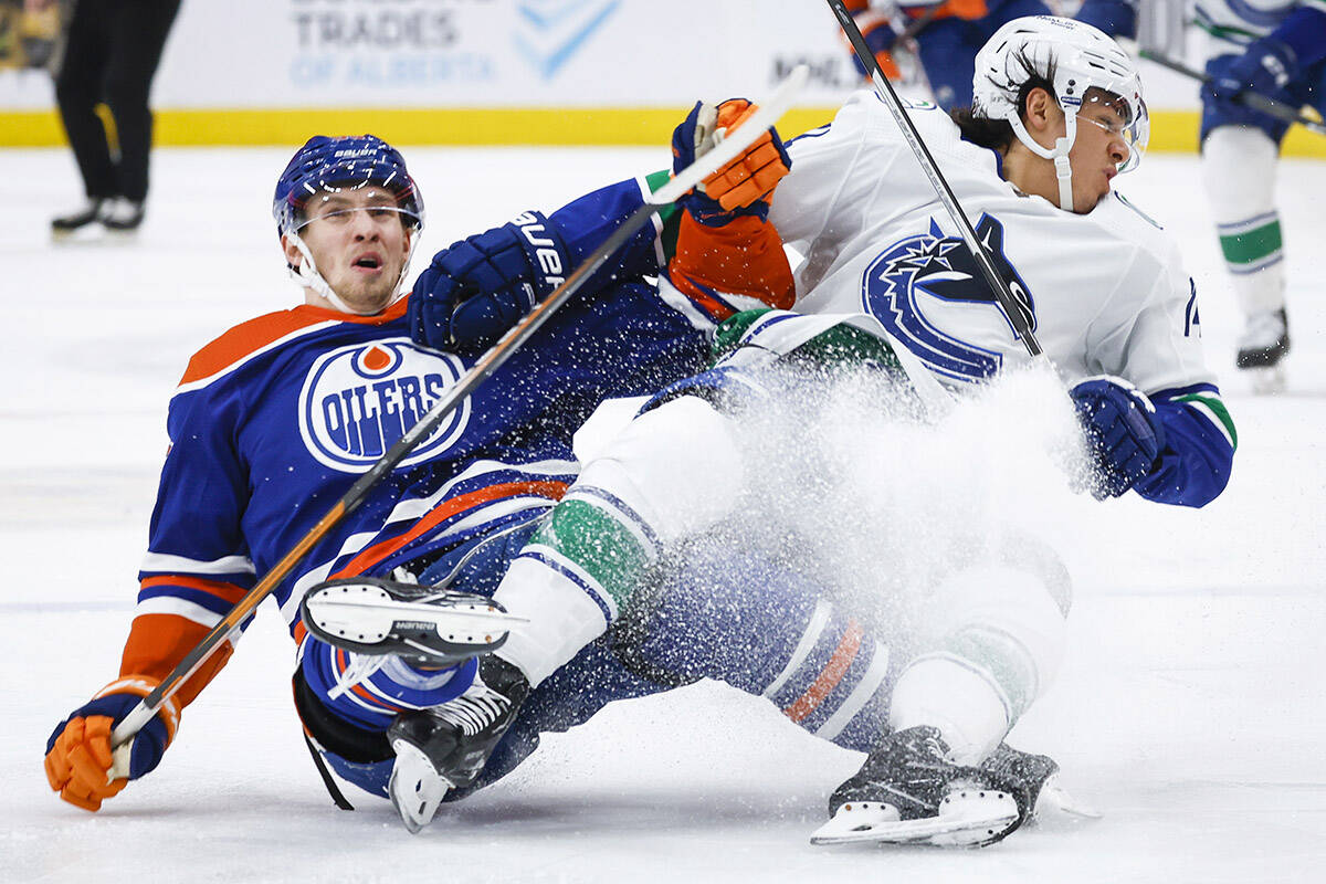 Vancouver Canucks defenceman Ethan Bear, right, is tripped by Edmonton Oilers forward Dylan Holloway during second period NHL hockey action in Edmonton, Friday, Dec. 23, 2022.THE CANADIAN PRESS/Jeff McIntosh