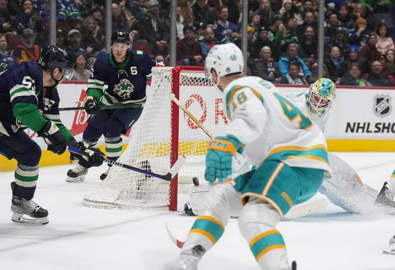Vancouver Canucks’ Bo Horvat, left, scores against San Jose Sharks goalie James Reimer, back right, during the first period of an NHL hockey game in Vancouver, on Tuesday, Dec. 27, 2022. THE CANADIAN PRESS/Darryl Dyck