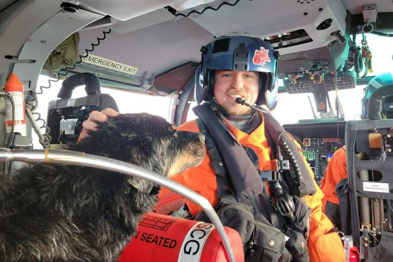 An unidentified member of the United States Coast Guard Air Station Port Angeles aircrew pets a dog on board his helicopter after the dog was airlifted from a sailboat that had washed onto rocks off Vancouver Island in a Wednesday, Dec. 28, 2022, handout photo. A sailor and his two dogs are recovering on Vancouver Island thanks to life-saving action by the USCG. THE CANADIAN PRESS/HO-United States Coast Guard