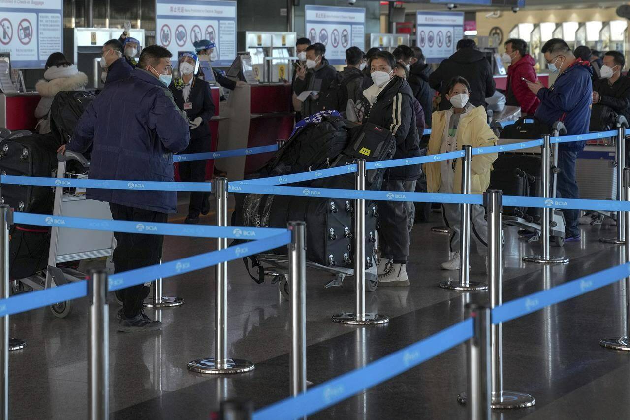 Masked travellers with luggage line up at the international flight check in counter at the Beijing Capital International Airport in Beijing, Thursday, Dec. 29, 2022. An expert says Canada’s requirement of a negative COVID-19 test of travellers from China will not help in preventing new variants or the spread of the virus. THE CANADIAN PRESS/AP/Andy Wong