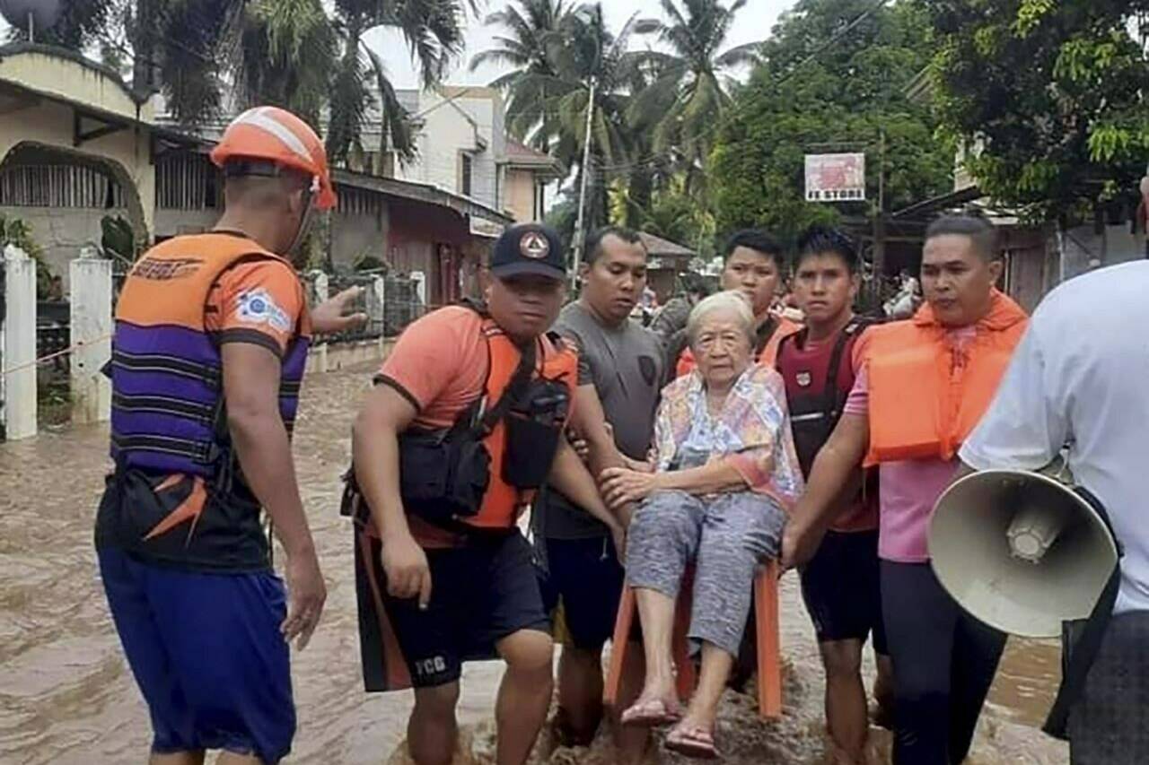 In this image provided by the Philippine Coast Guard, an elderly woman sits on a chair while being carried by coast guard personnel wading through floodwaters in Plaridel, Misamis Occidental province in the southern Philippines, Monday, Dec. 26, 2022. Heavy rains and floods devastated parts of the Philippines over the Christmas weekend. (Philippine Coast Guard via AP)