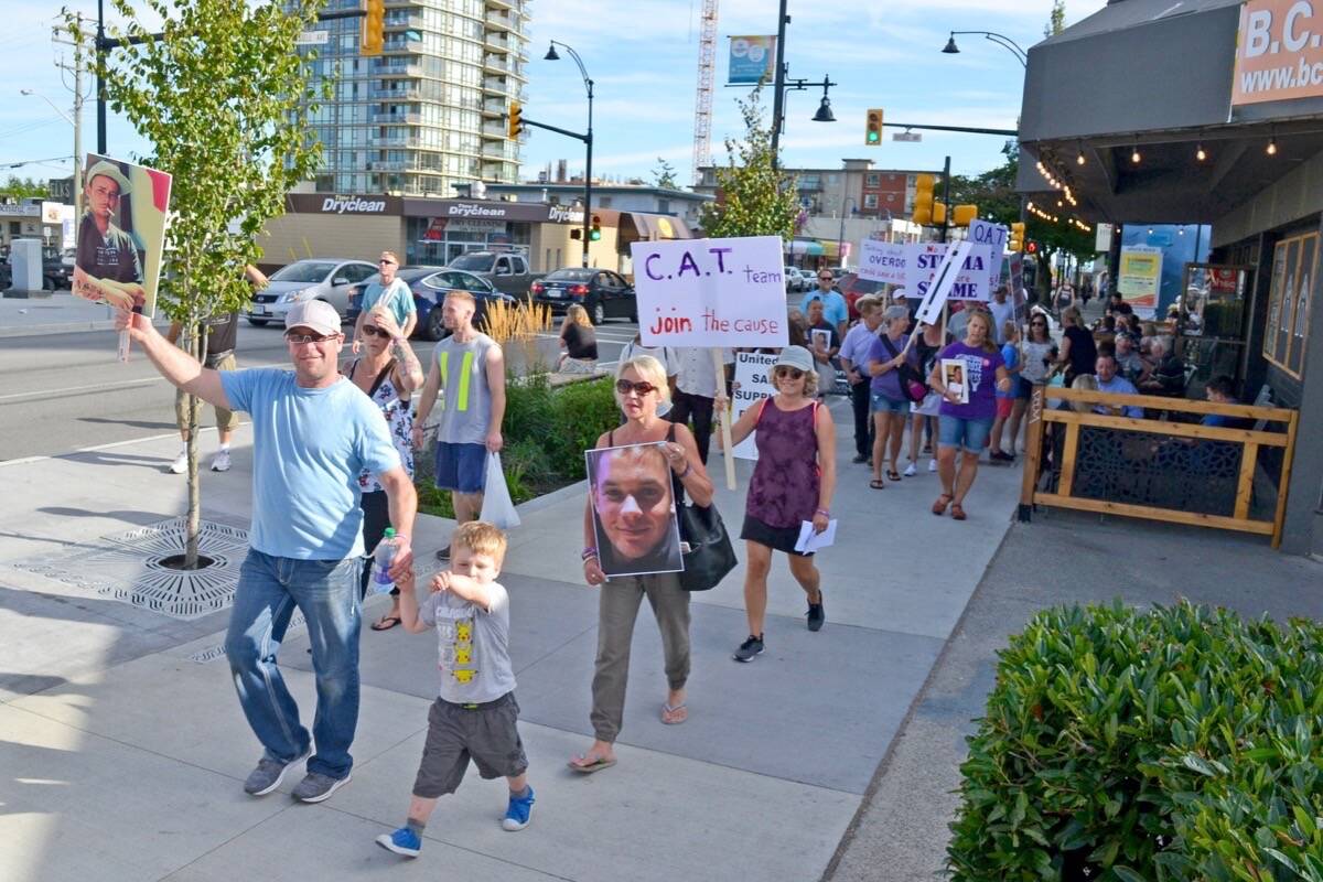 Back on Track recovery house operator Cole Izsak (left) and South Surrey parent Maggie Plett (holding a photo of her son, Zachary) walk north along White Rock’s Johnston Road with dozens of others in a 2019 effort to raise awareness around the overdose crisis. (Tracy Holmes file photo)