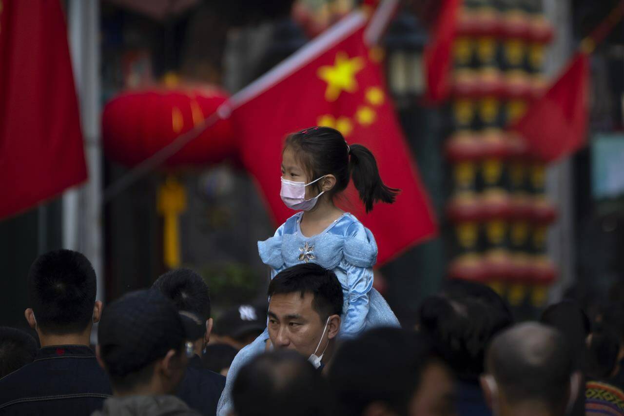 FILE - A girl wearing a face mask rides on a man’s shoulders as they walk along a tourist shopping street in Beijing on Oct. 7, 2022. China has announced its first overall population decline in recent years amid an aging society and plunging birthrate. (AP Photo/Mark Schiefelbein, File)