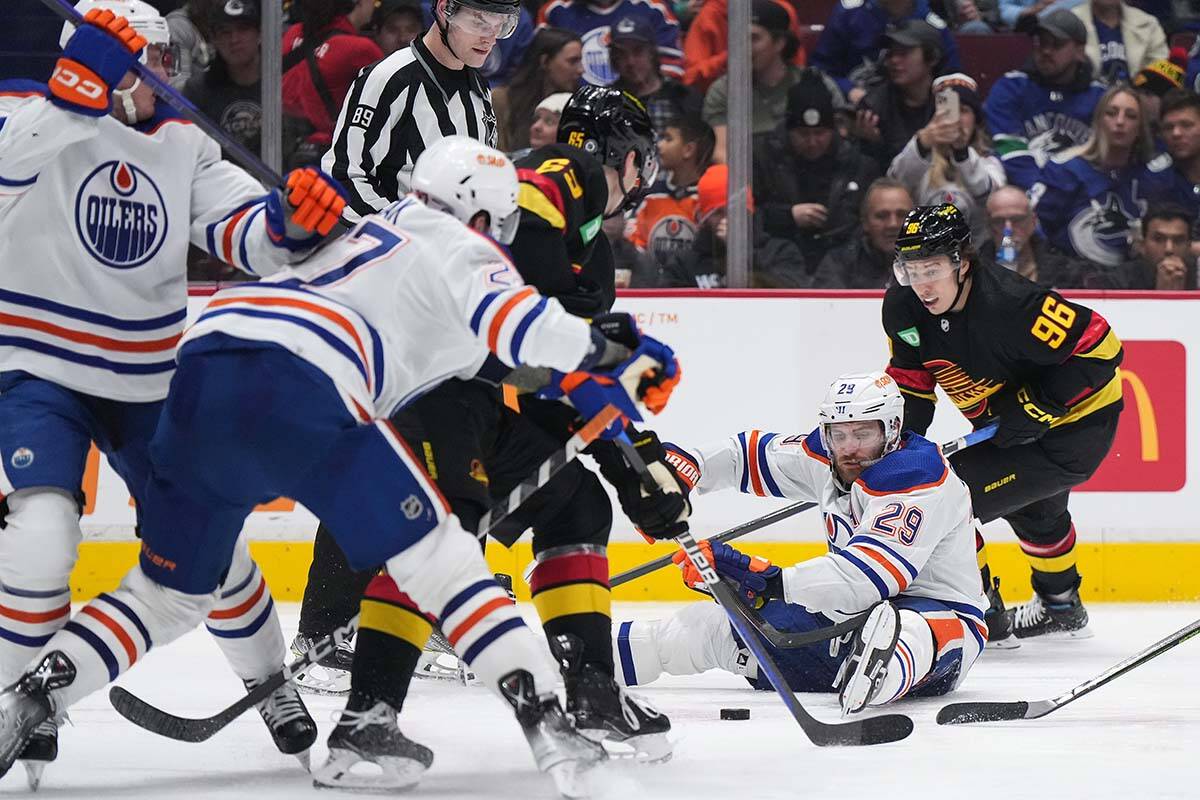 Edmonton Oilers Leon Draisaitl (29) plays the puck while sitting on the ice after falling in front of Vancouver Canucks Andrei Kuzmenko (96) during the third period of an NHL hockey game in Vancouver, on Saturday, January 21, 2023. THE CANADIAN PRESS/Darryl Dyck