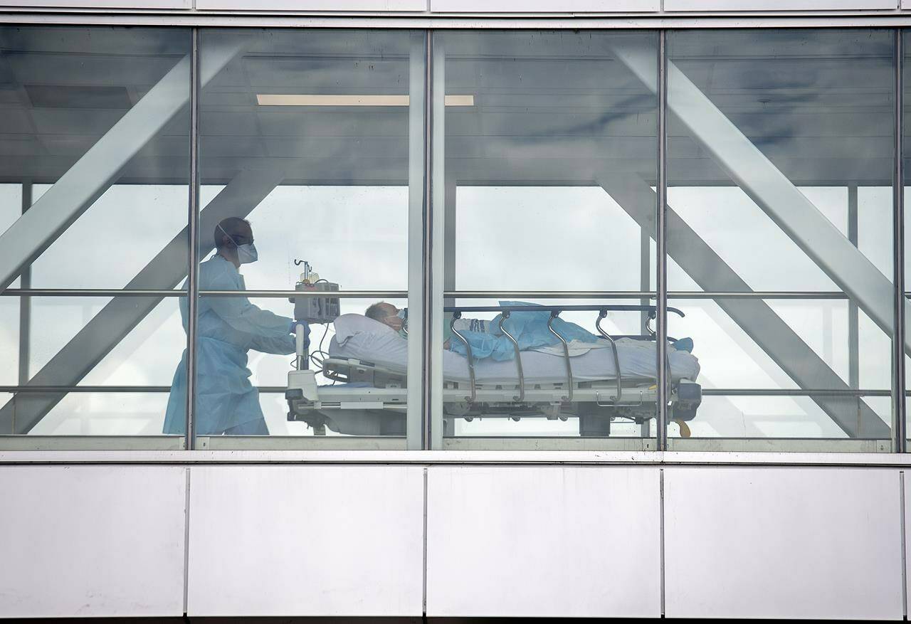 A health-care worker pushes a patient across a connecting bridge at a hospital in Montreal, Thursday, July 14, 2022. A new report says misinformation about COVID-19 contributed to more than 2,800 Canadian deaths and at least $300 million in hospital and ICU visits. THE CANADIAN PRESS/Graham Hughes
