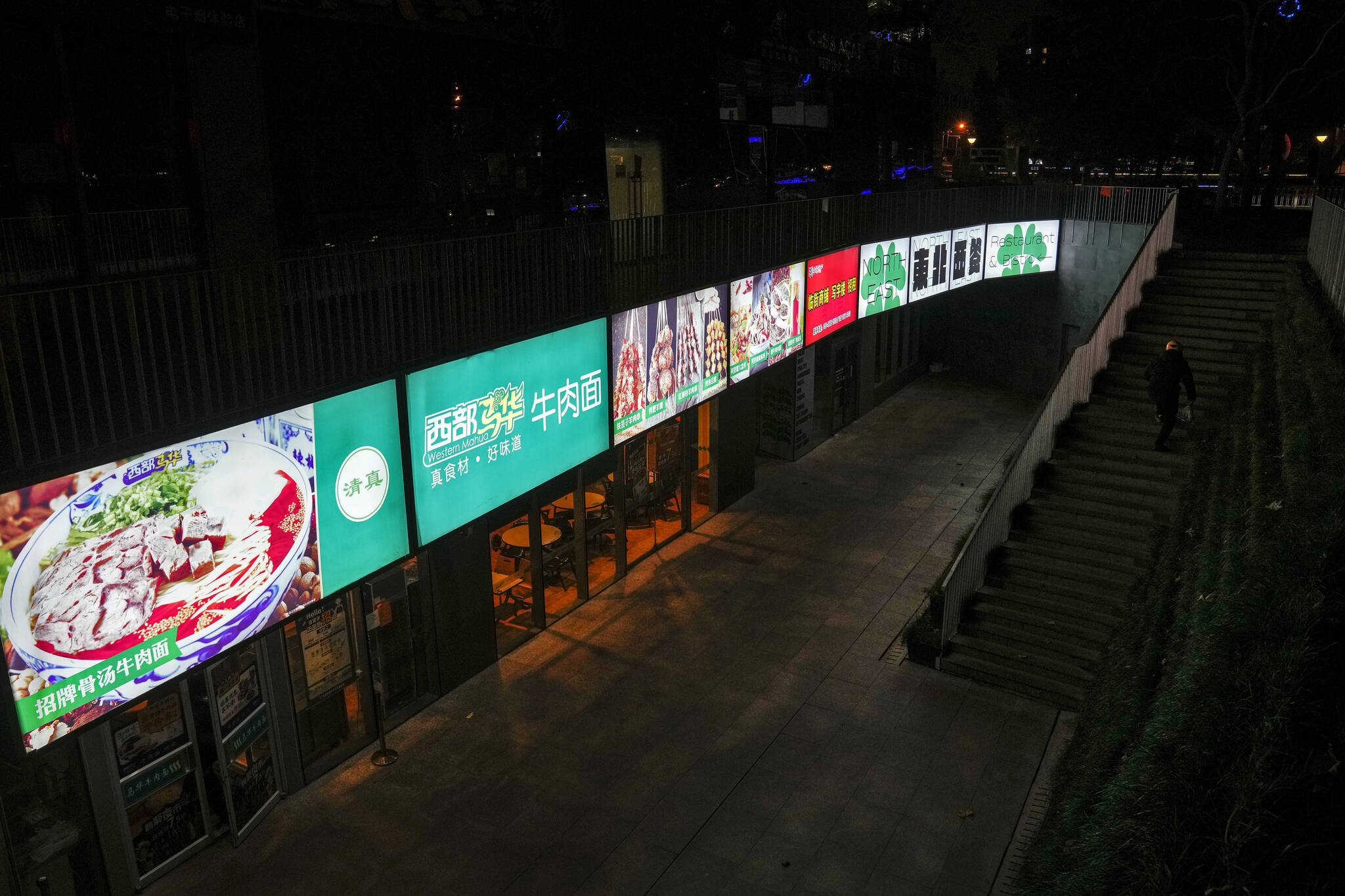 A food delivery rider walks up a staircase near restaurants only allowing take away in a shuttered commercial distirct as part of COVID-19 controls in Beijing, Tuesday, Nov. 22, 2022. (AP Photo/Andy Wong)