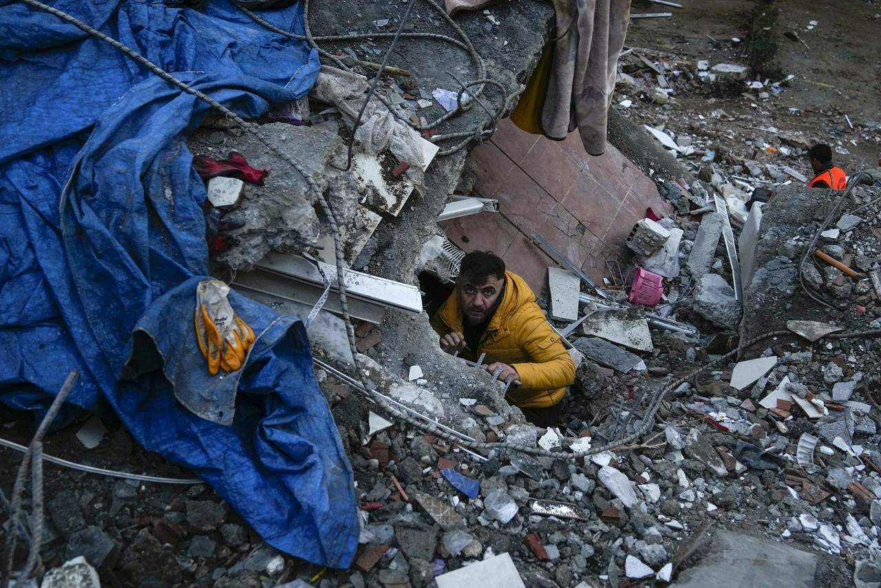 A man searches for people in a destroyed building in Adana, Turkey, Monday, Feb. 6, 2023. A powerful quake has knocked down multiple buildings in southeast Turkey and Syria and many casualties are feared. (AP Photo/Khalil Hamra)