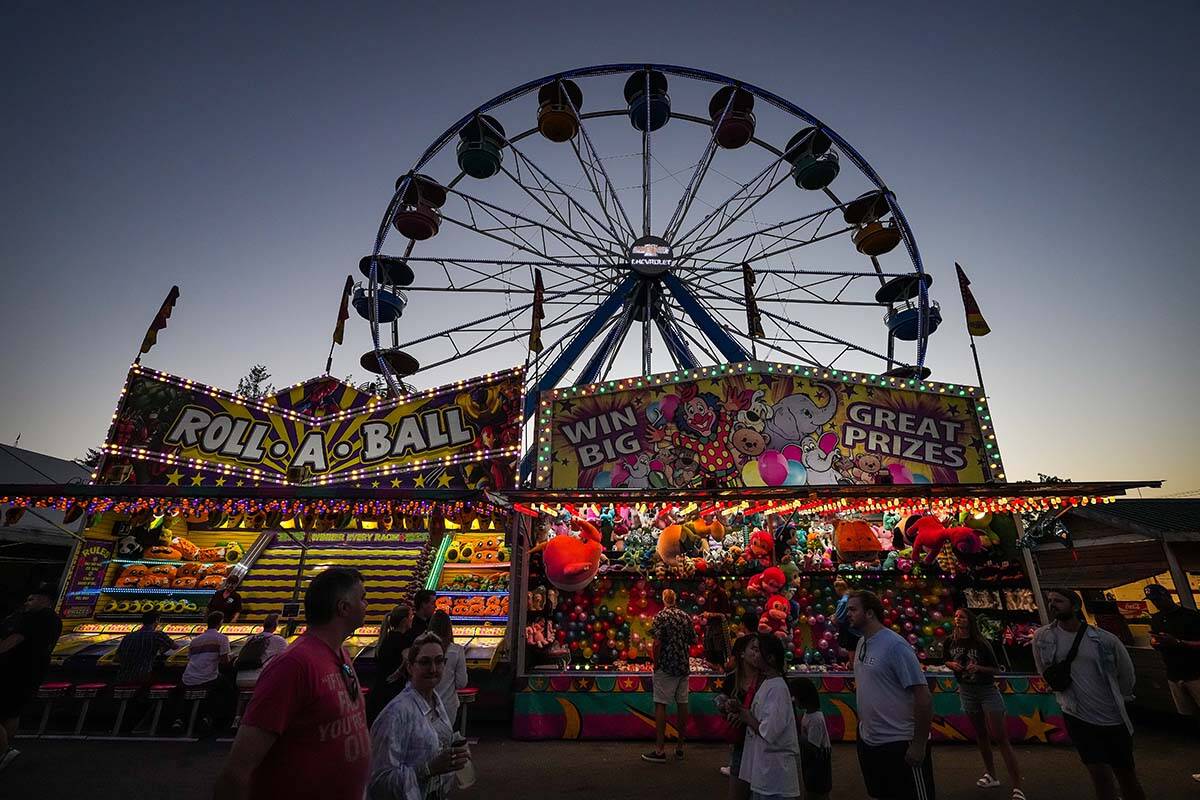 People walk past carnival game stands below a ferris wheel during the Pacific National Exhibition Fair, in Vancouver, on Thursday, September 1, 2022. THE CANADIAN PRESS/Darryl Dyck