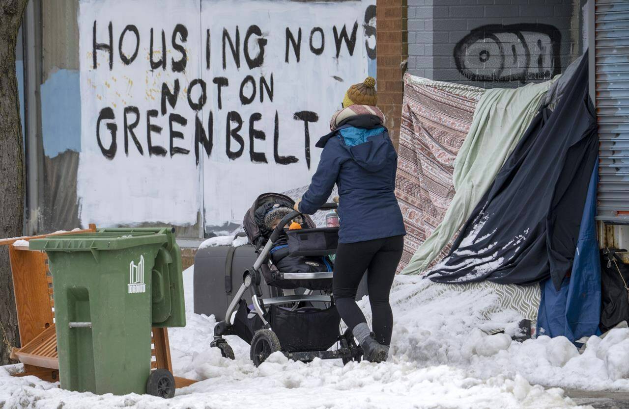 A person pushes a stroller past the shelter of an unhoused person in Toronto on Tuesday Jan. 31, 2023. The federal housing advocate is launching a review of homeless encampments in Canada, calling the situation a human rights crisis fuelled in part by the failure of all levels of government to provide adequate housing. THE CANADIAN PRESS/Frank Gunn