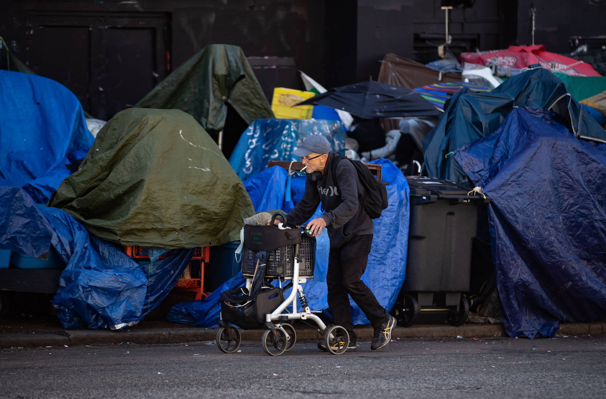 A man using a rolling walker walks on the street past tents setup on the sidewalk at a sprawling homeless encampment on East Hastings Street in the Downtown Eastside of Vancouver, on Tuesday, August 16, 2022. The cityÕs fire chief issued an order last month requiring the tents to be cleared because of an extreme fire safety hazard. THE CANADIAN PRESS/Darryl Dyck