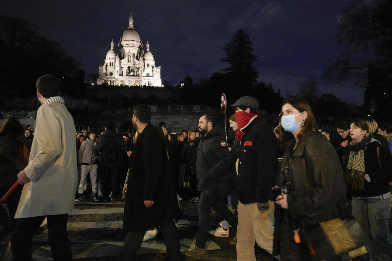 Protesters pass by the Montmartre Sacré-Coeur Basilica during a protest in Paris, Wednesday, March 22, 2023. Macron said Wednesday that the pension bill he pushed through without a vote in parliament needs to be implemented by the “end of the year,” sticking to his decision to raise the retirement age from 62 to 64 despite mass protests. (AP Photo/Lewis Joly)