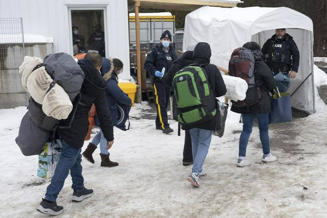 A family of asylum seekers from Colombia is met by RCMP officers after crossing the border at Roxham Road into Canada from Champlain, New York, Thursday, Feb. 9, 2023. Immigration advocates say they are disappointed that Canada and the U.S. have agreed to restrict the flow of asylum seekers across their shared border. THE CANADIAN PRESS/Ryan Remiorz