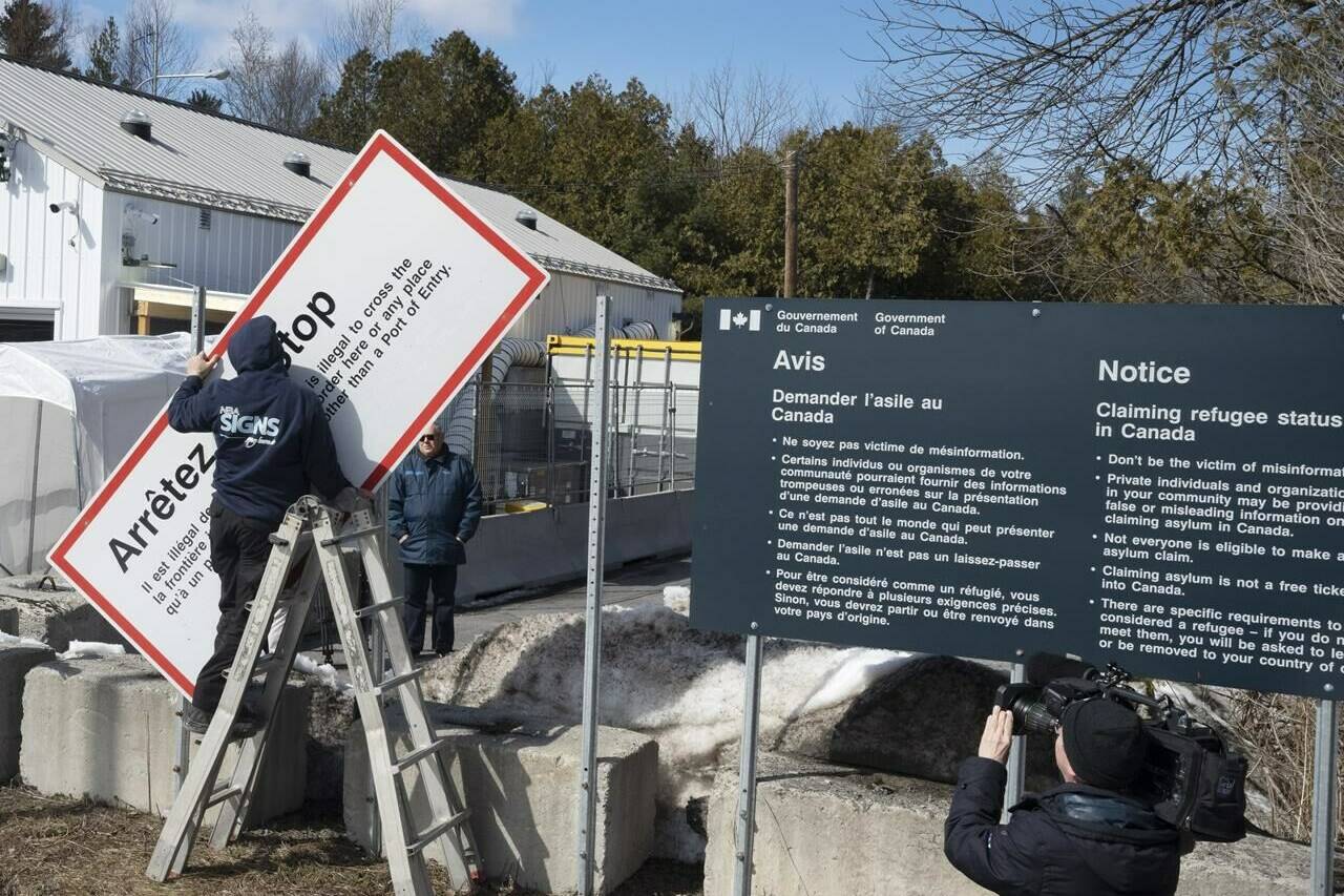 Workers remove warning signs at the irregular border at Roxham Road from New York into Canada on Friday, March 24, 2023, in Champlain, N.Y. THE CANADIAN PRESS/Ryan Remiorz