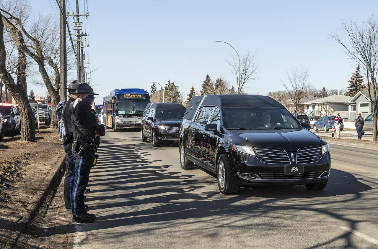 Police salute during a procession to a funeral home for Const. Travis Jordan and Const. Brett Ryan in Edmonton on Tuesday, March 21, 2023. A regimental funeral is set to be held Monday for the two officers, who were shot and killed while responding to a family dispute. THE CANADIAN PRESS/Jason Franson
