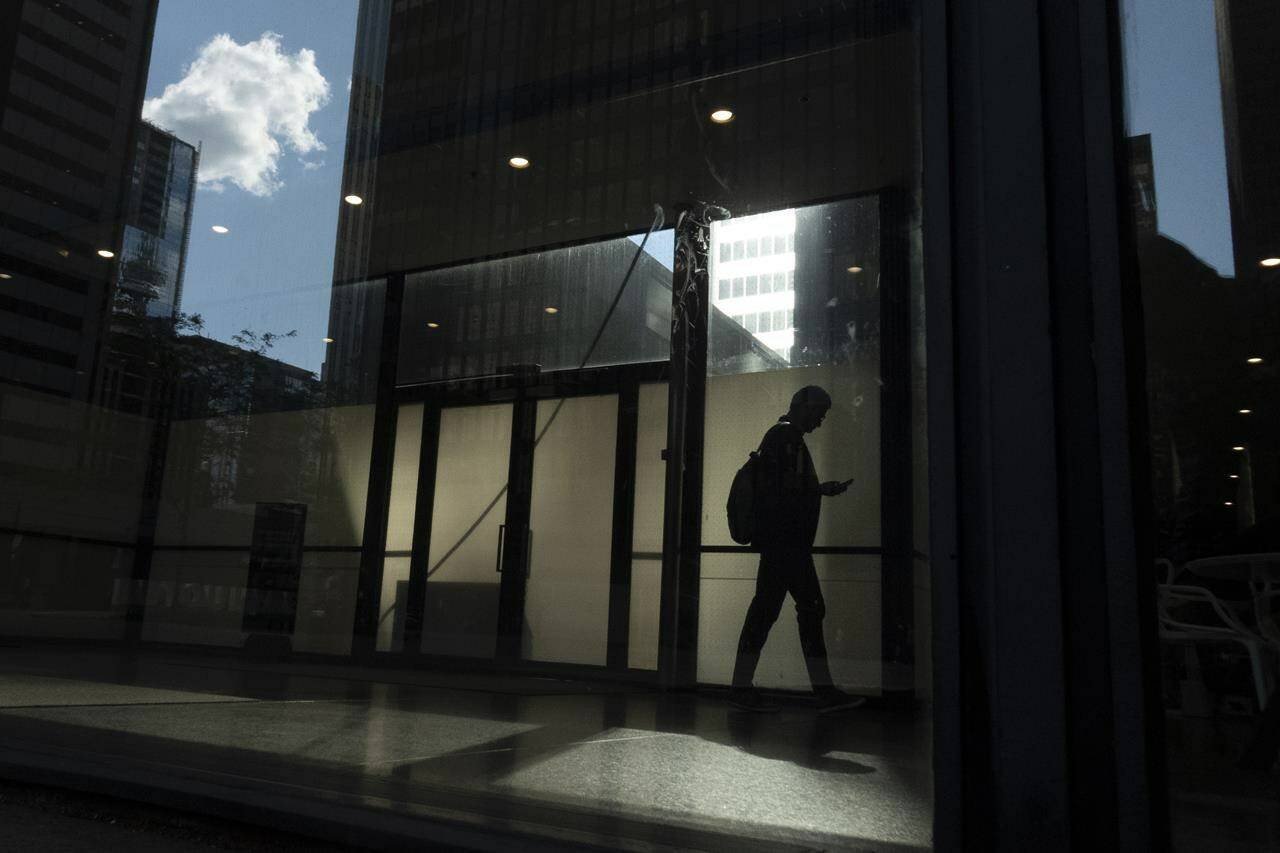 A man walks though a downtown Toronto office building with other buildings reflected in a window in this June 11, 2019 photo. The future of Canada’s social safety net is pending after the federal budget made no mention of employment insurance reform, despite the Liberals having promised to modernize the program. THE CANADIAN PRESS/Graeme Roy