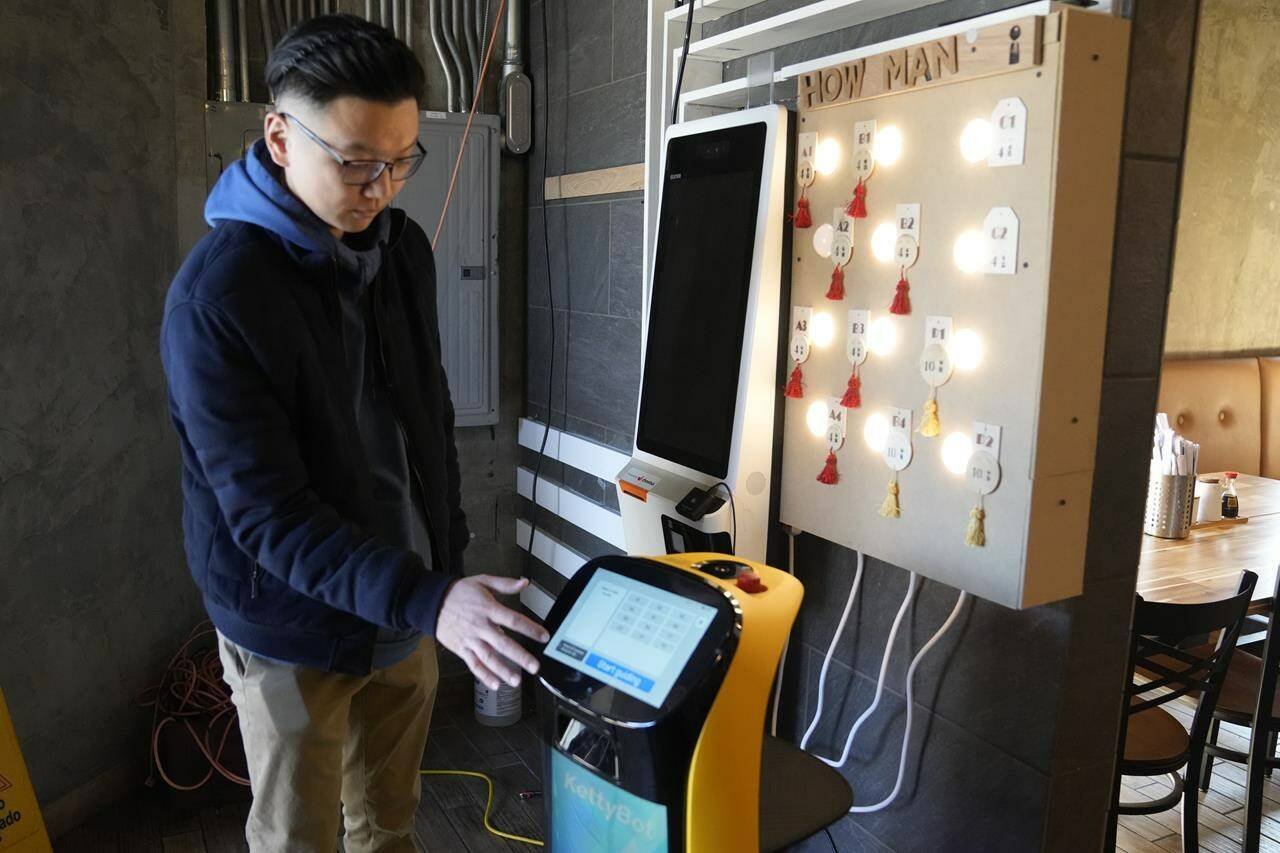 Li Zhai of the Noodle Topia restaurant points out features on his BellaBot robot, Monday, March 20, 2023 in Madison Heights, Mich. Zhai was having trouble finding staff for the restaurant in the summer of 2021, so he bought a robot which was so successful he added two more. With the robots, Zhai only needs three workers to do the same volume of business that five or six people used to handle. (AP Photo/Carlos Osorio)