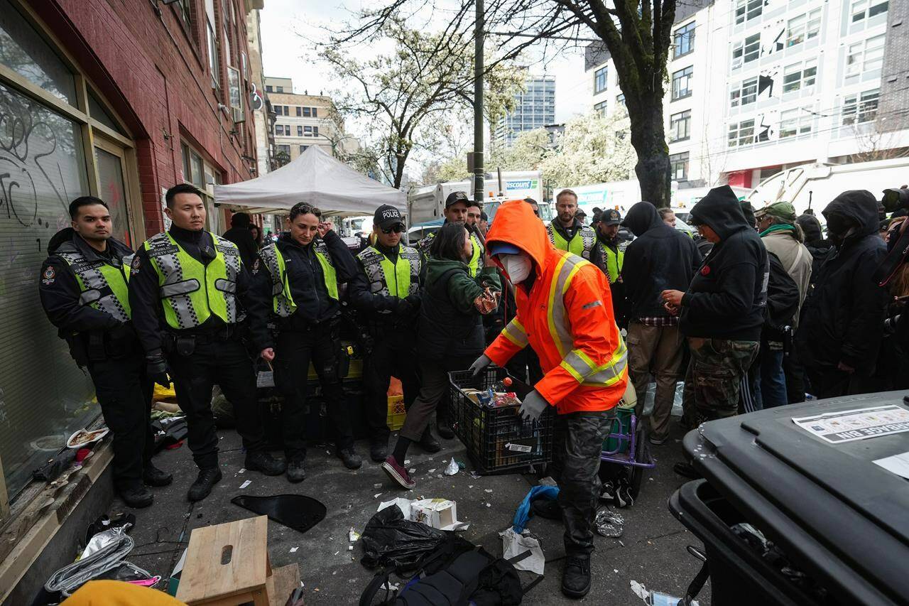 Vancouver police officers form a barricade as a person removes their belongings while city workers clear an encampment on East Hastings Street in the Downtown Eastside of Vancouver, on Wednesday, April 5, 2023. Vancouver police officers have been deployed to a tent encampment on the city’s Downtown Eastside with the aim of shutting down the site to campers. THE CANADIAN PRESS/Darryl Dyck