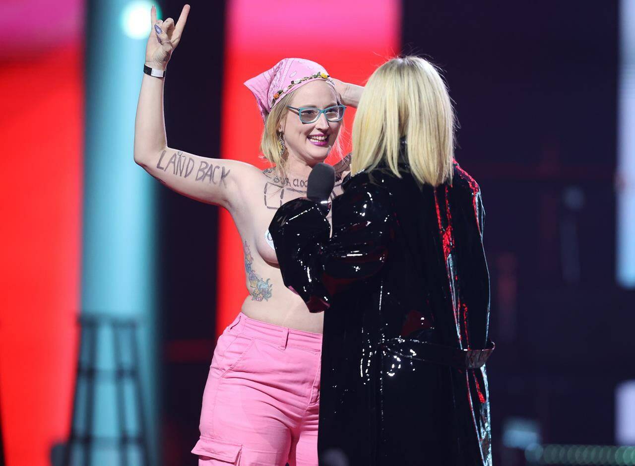 Avril Lavigne confronts a topless protester during the Junos on Monday, March 13, 2023. A climate change advocacy group says the woman who walked on the Juno Awards stage while topless has now sprayed pink paint on the entrance to the prime minister’s office in Ottawa. THE CANADIAN PRESS/Timothy Matwey