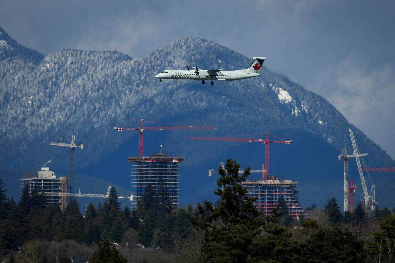An Air Canada Express aircraft on approach to land at Vancouver International Airport in Richmond, B.C., travels past construction cranes at the Oakridge Centre mall redevelopment in Vancouver, Tuesday, April 11, 2023. Officials with Vancouver International Airport are promising new real-time weather monitoring equipment, gate protocols and better communication after releasing a review of the travel chaos caused by snow last December. THE CANADIAN PRESS/Darryl Dyck